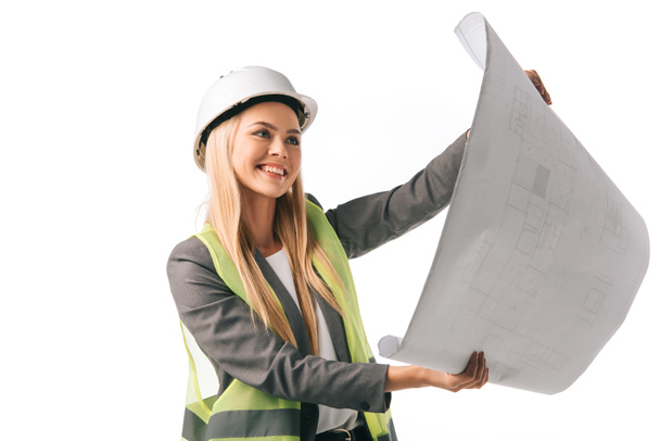 cheerful female architect in safety vest and hardhat working with blueprint, isolated on white - Foto, imagen