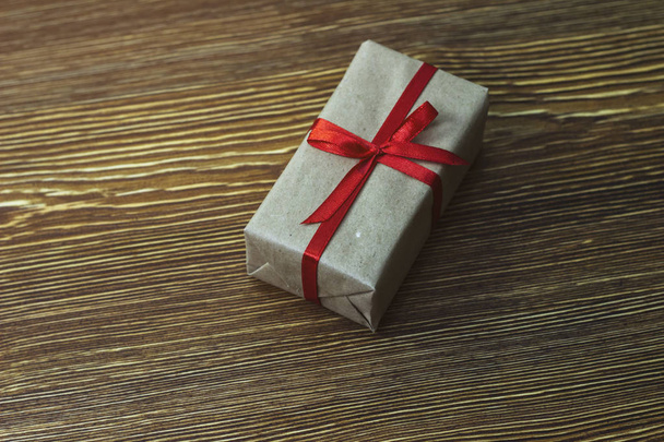A gift box with a red ribbon is on a wooden table - Foto, Bild