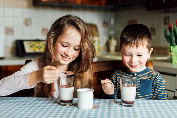 I bambini bevono latte in cucina al mattino. Sorella e fratello preparano il cacao
 - Foto, immagini