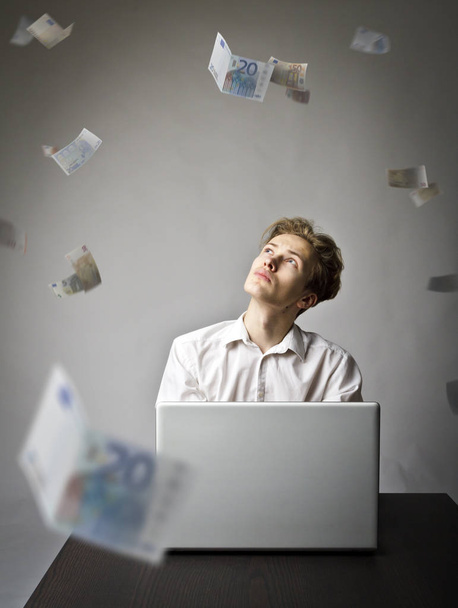 Young man using a laptop to browse the net. Young worker and falling Euro banknotes. Currency and job concept. - Photo, Image