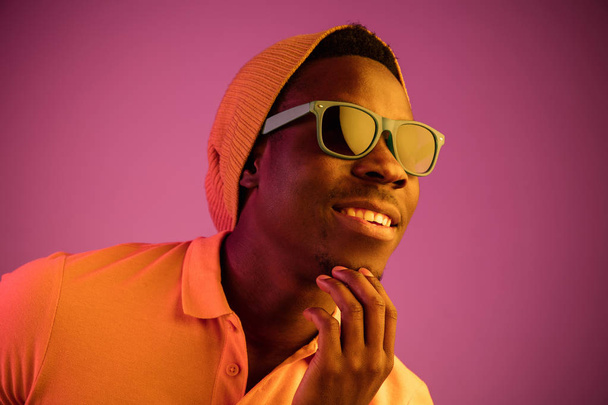 Portrait of a happy young african american man smiling on black neon background - Φωτογραφία, εικόνα