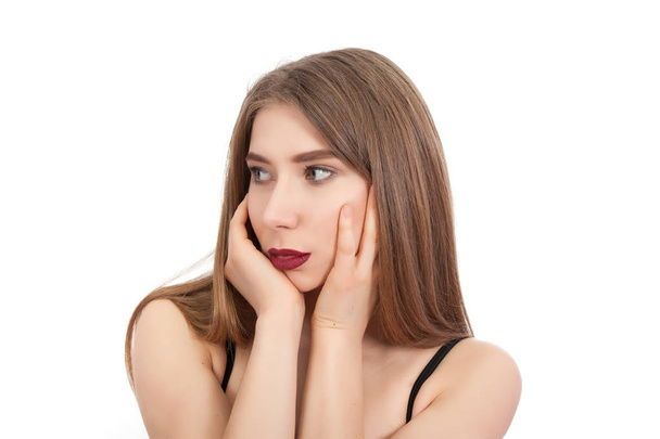 Portret van een jong mooi meisje met make-up geïsoleerd op een witte achtergrond. Een vrouw ziet er weg en houdt haar handen over haar gezicht. - Foto, afbeelding