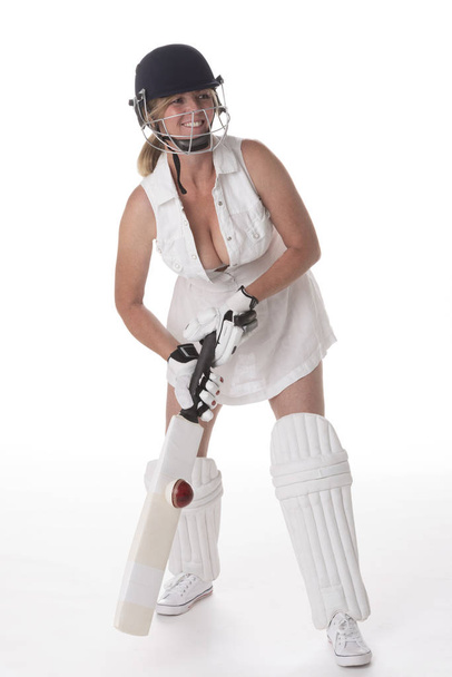 Cricketspielerin im weißen Kleid mit Schutzhelm, Schienbeinschoner, Schläger und Ball. - Foto, Bild