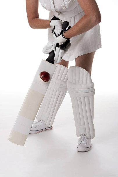 Mujer jugador de críquet en un vestido blanco con un casco de seguridad, espinilleras, un bate y una pelota
. - Foto, imagen