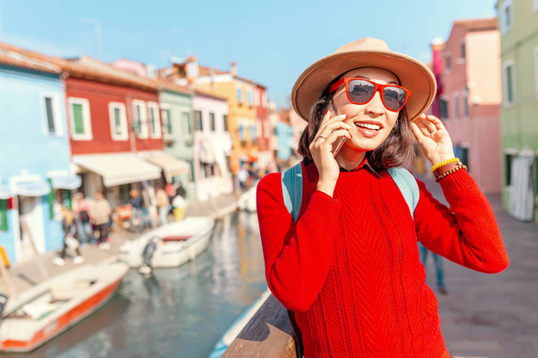 young happy traveler woman talking by phone among colorful houses on Burano island, Venice. Tourism in Italy concept - Photo, Image