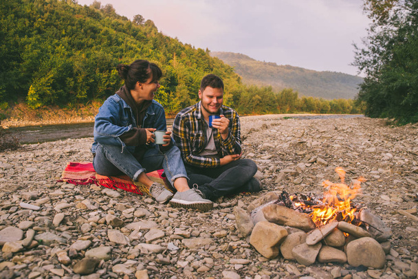 két fiatal pár campfire fel tea ivás meleg közelében ült és beszélt. életmód fogalom - Fotó, kép