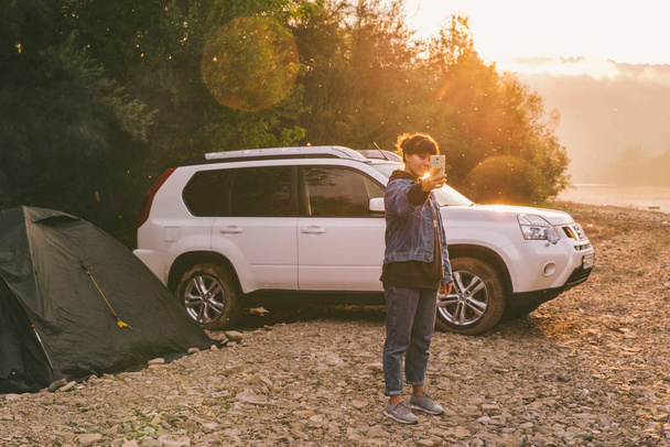 woman taking picture of sunrise on her phone. car camping. lifestyle concept - Photo, Image