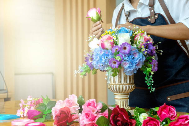 цветочный художник женщина работает, чтобы украсить искусственные цветы украсить на столе со многими цветами бумаги и пластиковых цветов
 - Фото, изображение