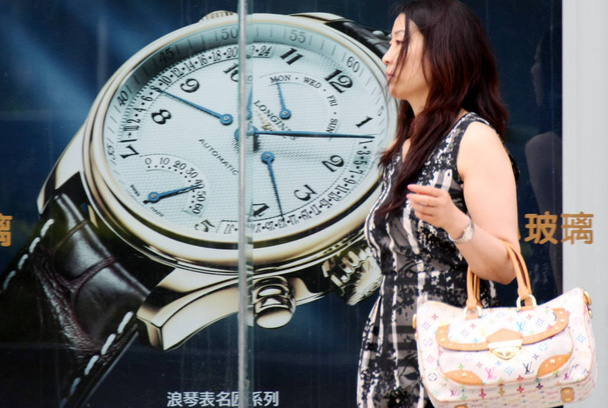 A Chinese woman carrying a Louis Vuitton (LV) bag walks past an advertisement for Longines watches in Qingdao city, east Chinas Shandong province, 13 July 2011 - Foto, Imagen