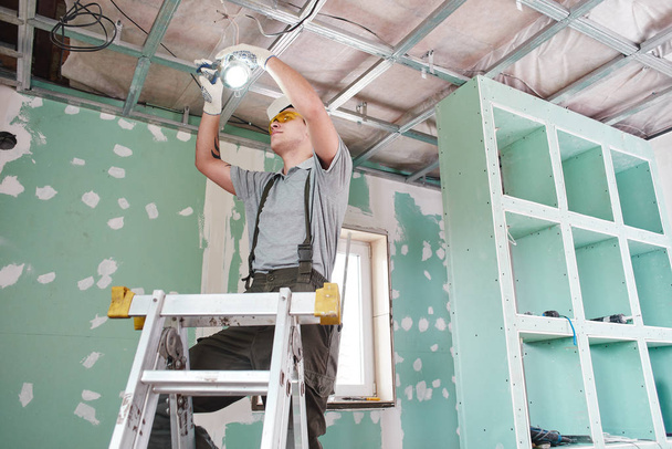 Room repair. Interior finish. young builder makes a plasterboard ceiling, standing on a stepladder - Photo, image