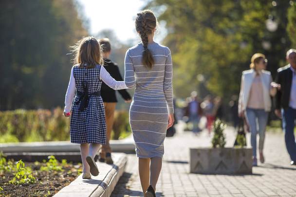 Widok dziewczyna dziecka i matki w sukienki razem trzymając się za ręce na ciepły dzień na zewnątrz w słoneczny tło z tyłu. - Zdjęcie, obraz