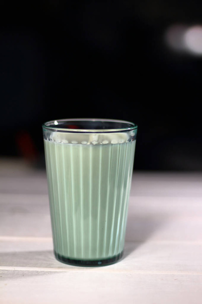 Um copo de leite em um copo de vidro facetado transparente em um fundo pretopreto
  - Foto, Imagem