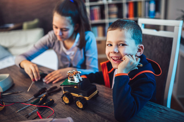 Щасливий усміхнений хлопчик і дівчинка створюють технічну іграшку і роблять робота. Технічна іграшка на столі повна деталей
 - Фото, зображення
