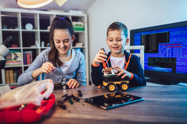 Счастливые улыбчивые мальчик и девочка, техническая игрушка и робот. Техническая игрушка на столе с деталями
 - Фото, изображение