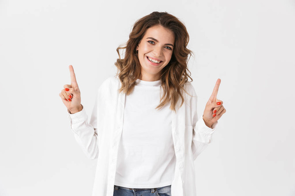 Portrait of positive woman in casual clothes pointing fingers upward isolated over white background - Foto, Imagem