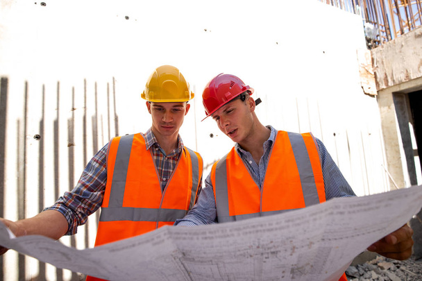 Gerente de construcción e ingeniero vestido con ropa de trabajo y sombreros duros explorar la documentación del proyecto en el sitio de construcción
 - Foto, Imagen