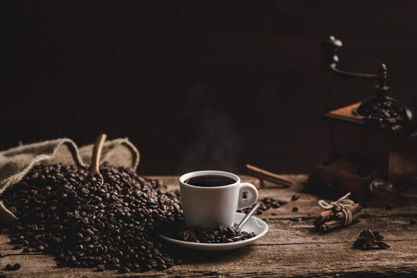 Kopje koffie bonen witte geurende koffie en koffiemolen op houten tafel op zwarte achtergrond - Foto, afbeelding