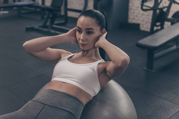Beautiful fit woman doing abs crunches on fitness ball, working out at the gym. Attractive fitness female exercising, doing abdominal crunches. Sportswoman training at gym studio. Sports, body care concept - Photo, Image