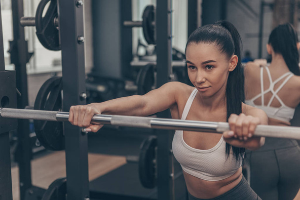 Confident young fitness woman looking concentrated, preparing for her barbell workout. Beautiful healthy female athlete focusing before lifting weights at gym sports studio, copy space - Foto, Imagem