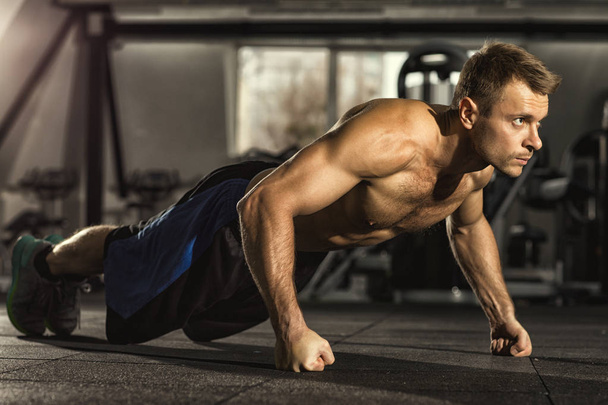 Pushing his limits. Full length shot of a shirtless man with toned muscular athletic body doing pushups working out at the gym confidence agility strength competition sports training concept - Фото, зображення