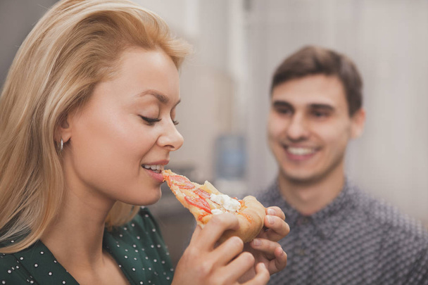 Крупним планом красива жінка їсть піцу, її гарний хлопець посміхається їй. Чудова жінка їсть замовила піцу, насолоджуючись романтичним домашнім вечором зі своїм чоловіком. концепція продовольчого обслуговування
 - Фото, зображення