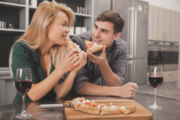Mladý pár se na sebe dívali s láskou, jíst pizzu na romantickou večeři doma, kopírovat prostoru. Šťastný manžel a manželka těší výborné jídlo v jejich bytě. Jídlo, valentinky koncept - Fotografie, Obrázek