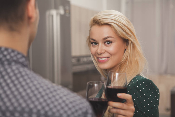 見事な幸せなブロンド髪若い女、カメラに笑顔男は彼女とロマンチックな夜を持っている赤ワインのガラスを保持しています。ワインを飲みながら周年を祝う幸せなカップル。愛の概念 - 写真・画像
