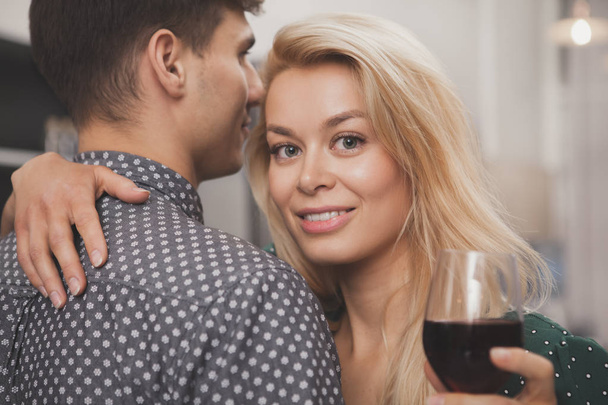 Belle jeune femme souriant à la caméra, embrassant son homme à la cuisine. Aimer couple embrasser, boire du vin, profiter de célébrer l'anniversaire. Relations, toasts, acclamations concept
 - Photo, image