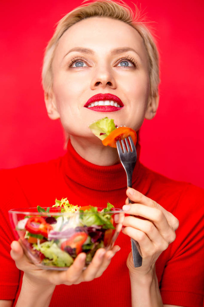 Gyönyörű kaukázusi nő eszik saláta, piros háttér felett - Fotó, kép