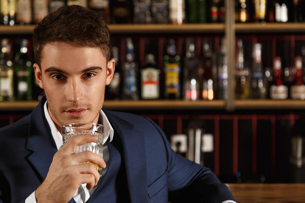 Share a drink with me. Closeup portrait of a handsome guy holding a whiskey glass looking at the camera seductively copyspace  - Zdjęcie, obraz