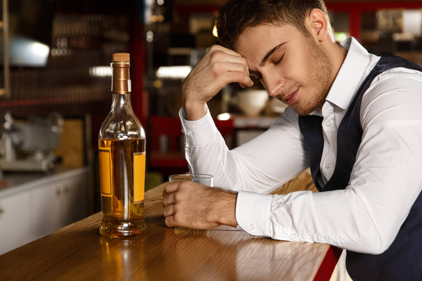 No company needed. Shot of a young handsome guy enjoying a quiet evening at the bar having whiskey smiling with his eyes closed  - Photo, image