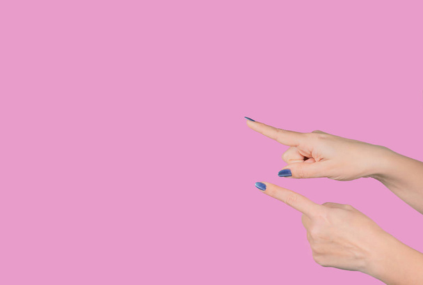 Vista de cerca de dos hermosas manos femeninas apuntando con sus dedos índice a algo virtual e invisible aislado sobre fondo rosa. Fotografía horizontal en color
. - Foto, imagen