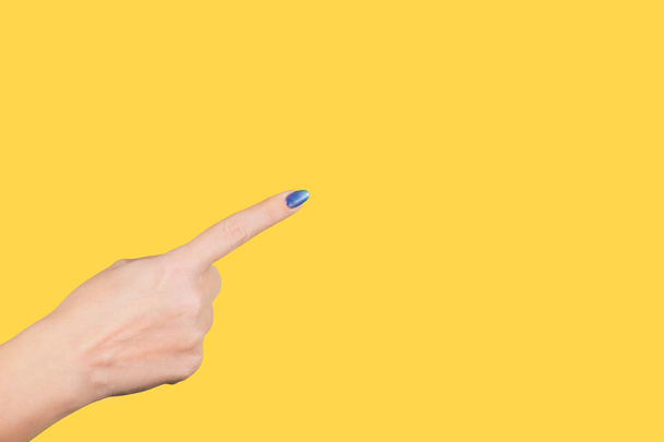 Close-up beeld van prachtige vrouwelijke hand virtuele en onzichtbare geïsoleerd op gele lichte achtergrond met haar wijsvinger op iets te wijzen. Horizontale kleurenfotografie. - Foto, afbeelding