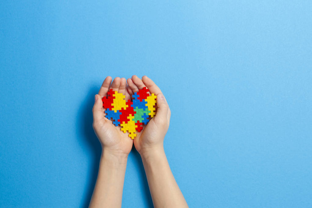 Child hand holding colorful heart on blue background. World autism awareness day concept - Photo, Image