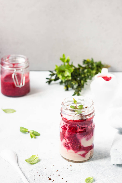 Tasty cottage cheese parfait with raspberry sauce and mint in a glass jar. Diet dessert. Light grey stone concrete background. Copy space. - Photo, image