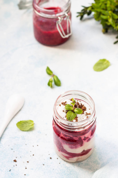 Tasty cottage cheese parfait with raspberry sauce and mint in a glass jar. Diet dessert. Light grey stone concrete background. Copy space. - Foto, immagini