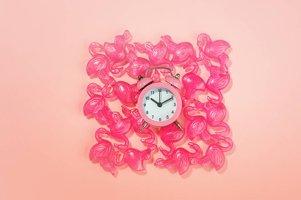 Alarm clock and pink flamingo toys on pastel pink coral background. Flamingo time for rest and relax. Creative layout concept gift party for birthday. Minimal summer concept with copy space, top view - Φωτογραφία, εικόνα