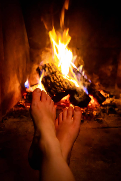 Γυμνά πόδια νεαρή γυναίκα θερμαίνεται από το τζάκι σε τζάκι - Φωτογραφία, εικόνα