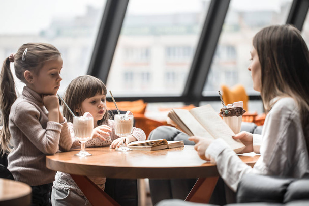 Счастливые молодые женщины мать с детьми, сидя за обеденным столом и разговаривая в ресторане или кафе. Отдых и общение с детским рестораном
 - Фото, изображение