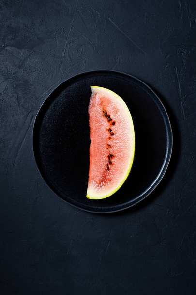 Une tranche de pastèque sur une assiette noire. Fond sombre, vue de dessus
 - Photo, image