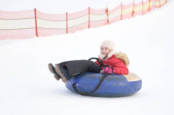 Ευτυχισμένο κοριτσάκι που κατεβαίνει το λόφο σ 'ένα χιονισμένο πάρκο - Φωτογραφία, εικόνα