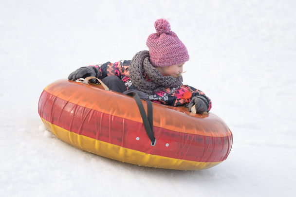 glückliches kleines Mädchen beim Rodeln den Hügel hinunter in einem verschneiten Park - Foto, Bild