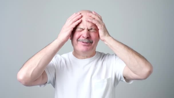 Hombre maduro en camiseta blanca con los ojos cerrados tocando su cabeza con dolor
. - Metraje, vídeo