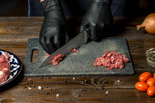 手袋で料理人の手では、基板の赤肉をカットします。トマト、タマネギ、バター、近くには。水平フレーム - 写真・画像