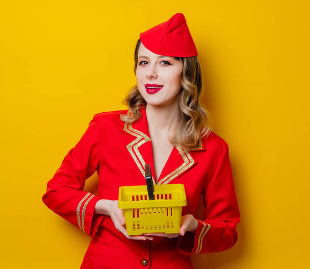 Портрет чарівної старовинної стюардеси в червоній формі з кошиком для покупок. Ізольовані на жовтому тлі
. - Фото, зображення