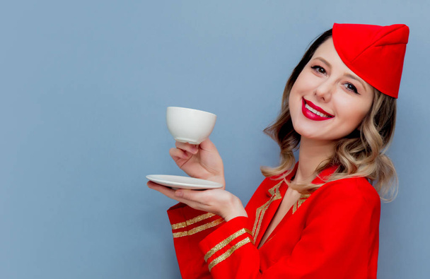 Portrait of charming vintage stewardess wearing in red uniform with cup of coffee or tea. Isolated on gray background. - Fotó, kép