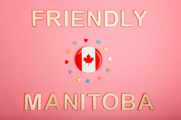 Cartão de felicitações Feliz Dia do Canadá com letras de madeira. Manitoba slogan licença provincial dizendo selvagem rosa país e bandeira canadense com muitos corações em coral vivo fundo rosa
.  - Foto, Imagem