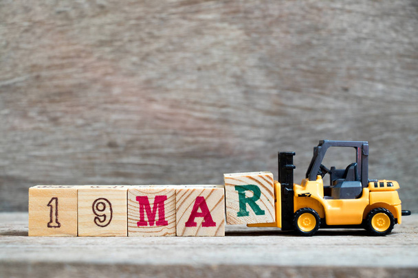 Toy forklift hold block R to complete word 19mar on wood background (Concept for calendar date 19 in month March) - Photo, Image
