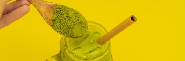 Lata de té verde con hielo en tarro de albañil y paja y cuchara con matcha en polvo sobre fondo amarillo. Té helado hecho en casa Matcha Latte con leche cero residuos BANNER, FORMATO LARGO
 - Foto, imagen