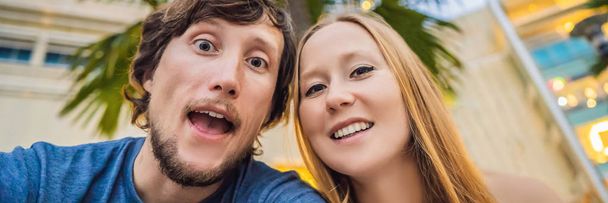Travel, vacation and holiday concept - Happy couple having fun taking selfie over park with palms background and skyscrapers BANNER, LONG FORMAT - Fotografie, Obrázek
